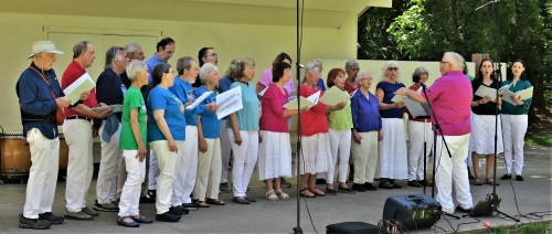 Single line of 25 choir members performing on stage with Jerry Campbell directing